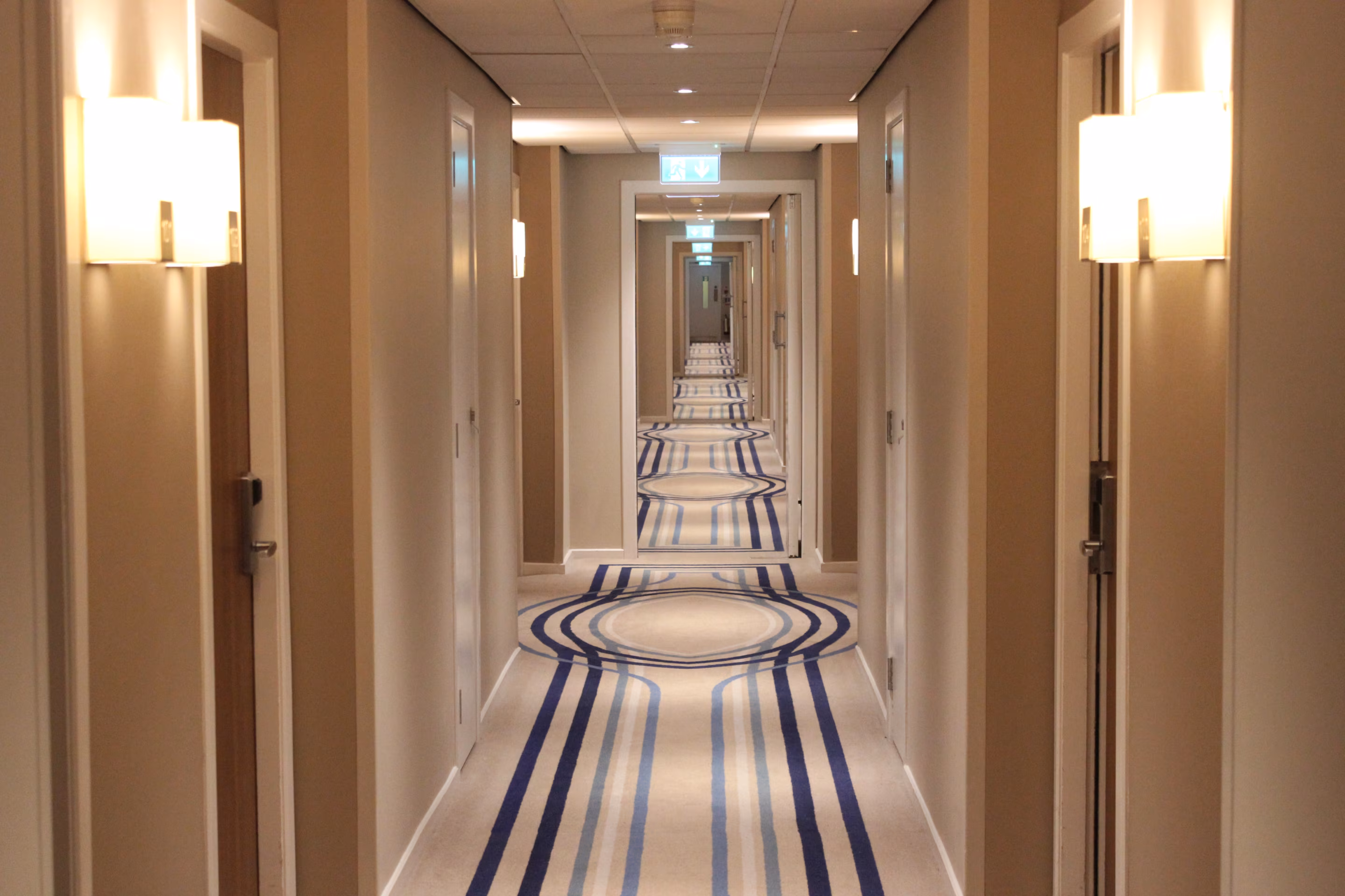 Hotelflur mit hellem Teppichboden mit blauen Streifen und Kreismuster vor den Zimmertüren