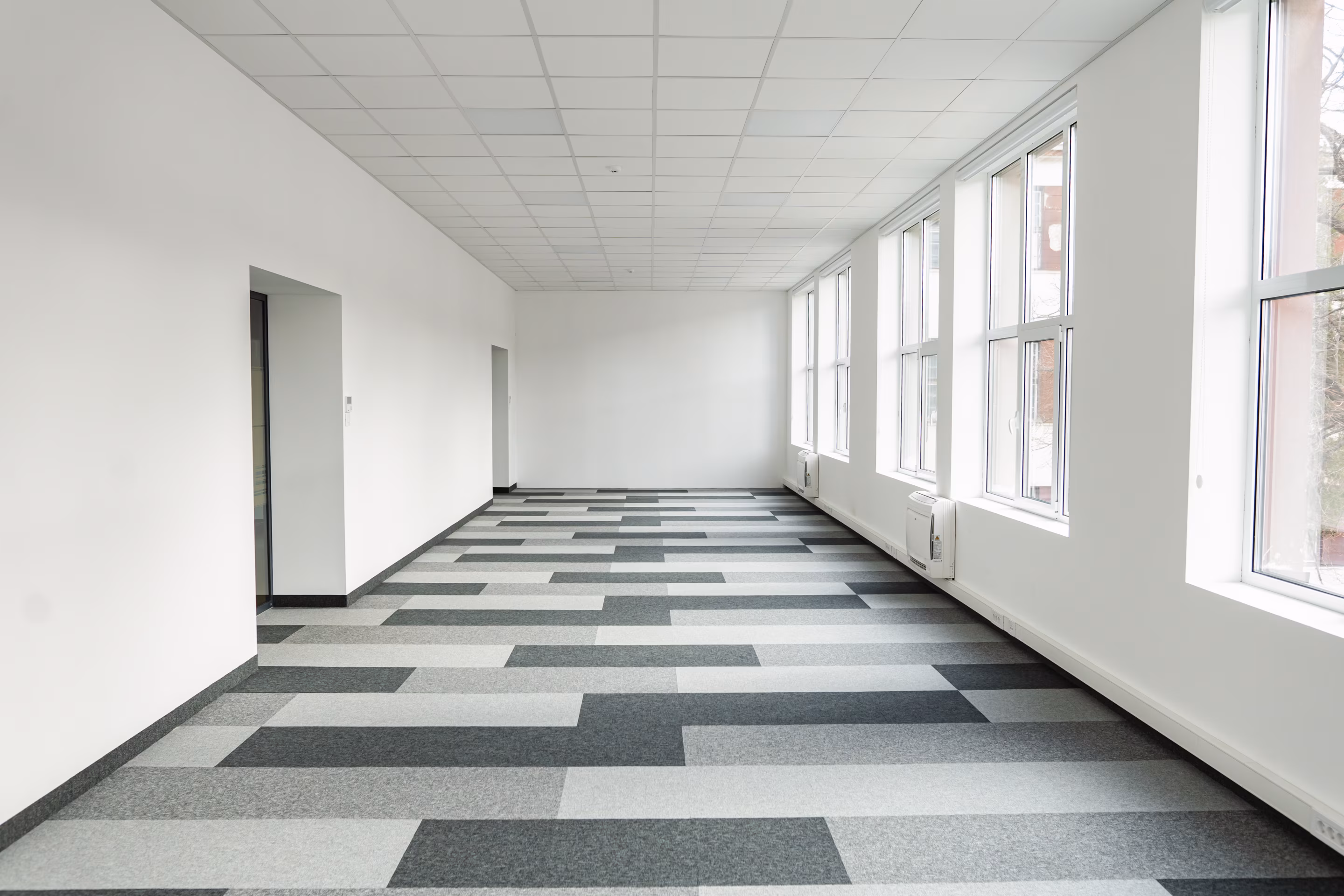 Leere Büroetage mit hellen Fensterfronten und Teppichfliesen in Grau- und Weißtönen